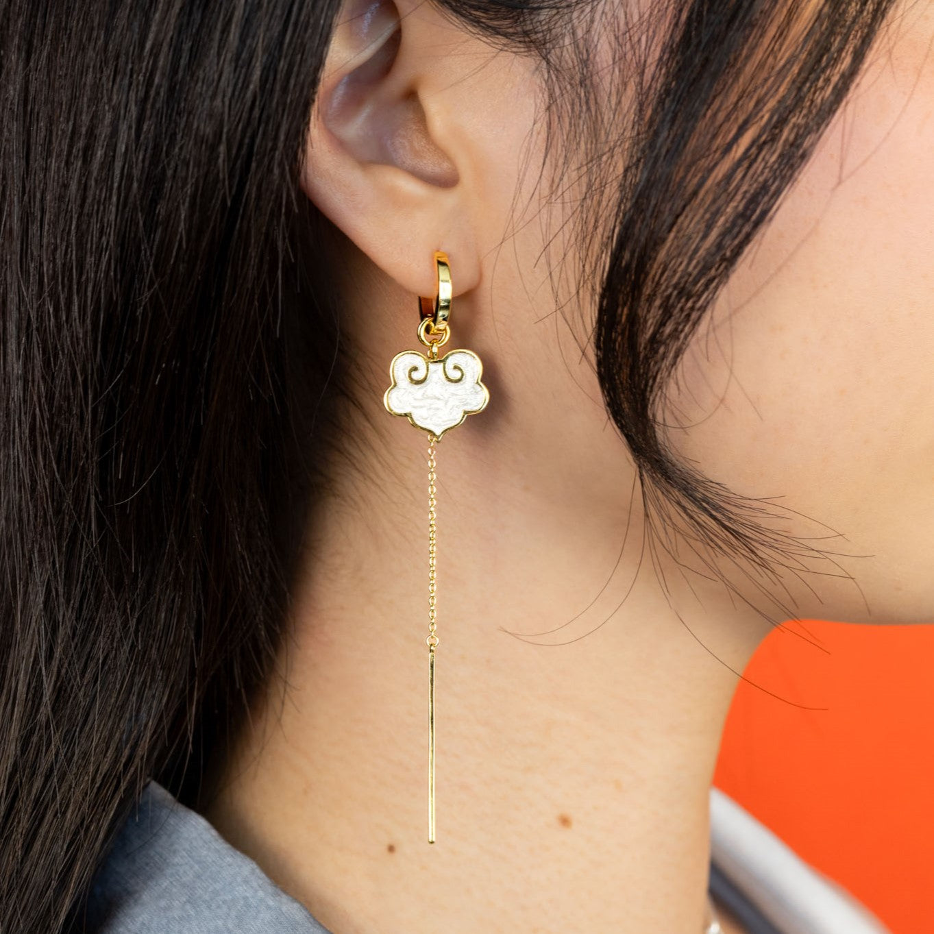 On model ruyi earrings with ruyi shaped charms outlined in gold and filled with pearlescent white enamel.