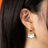 On model ruyi earrings with ruyi shaped charms outlined in gold and filled with pearlescent white enamel.