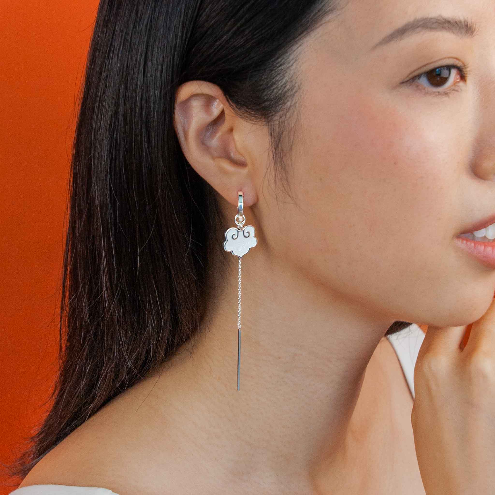 On model ruyi earrings with ruyi shaped charms outlined in silver and filled with pearlescent white enamel. 