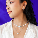 Woman modeling the Mini Mooncake Locket in silver styled with other silver jewelry.