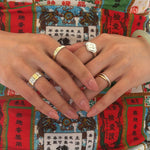 A close-up of two hands wearing several modern Chinese-inspired rings that are in gold, silver, and two-tone.