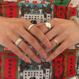 A close-up of two hands wearing several modern Chinese-inspired rings that are in gold, silver, and two-tone.
